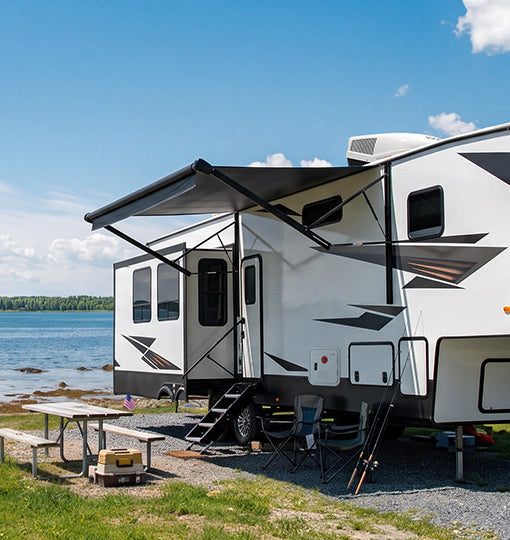 An RV parked beside a serene lake, surrounded by trees and misty fog, showcasing a peaceful outdoor setting.