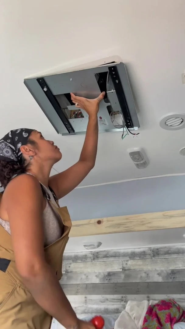 An installer supporting a Fogatti air-conditioner ceiling assembly inside an RV bedroom.