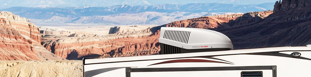 A white camper with a black roof parked against a mountainous backdrop, showcasing a fogatti air conditioner on the roof.