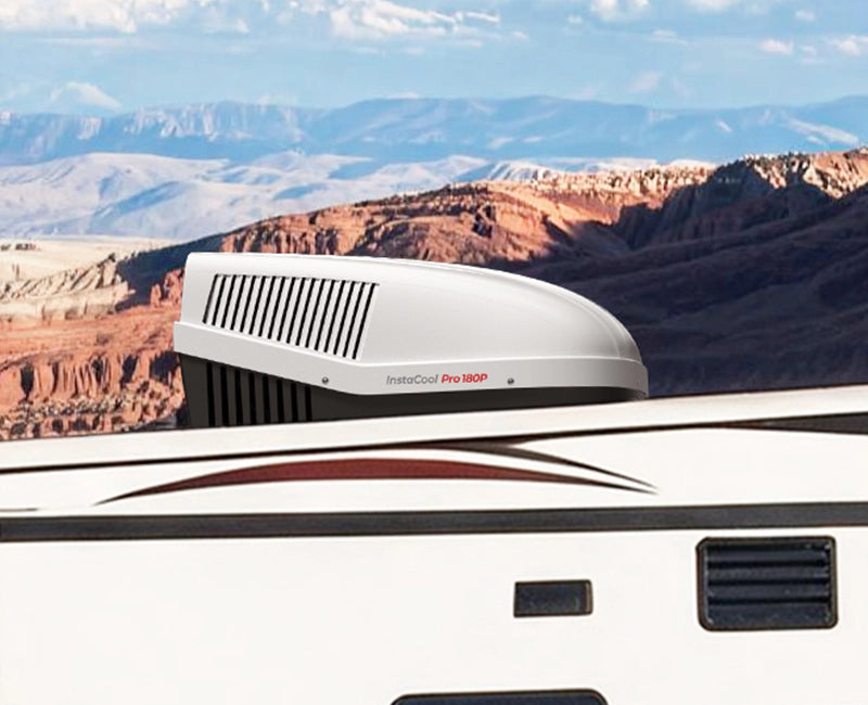 A white camper with a black roof parked against a mountainous backdrop, showcasing a fogatti air conditioner on the roof.